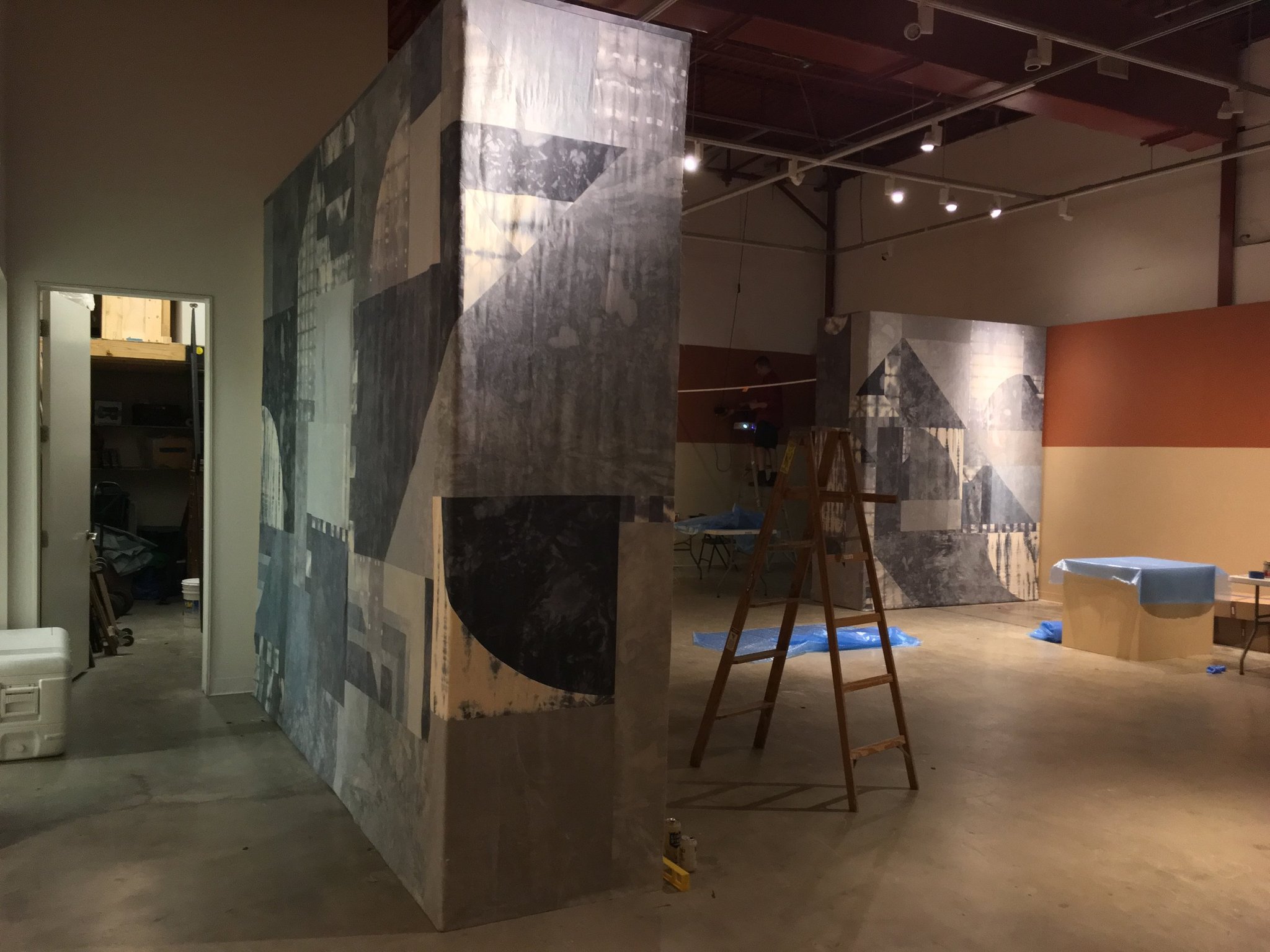 Art gallery installation in progress with large abstract wall panels and ladder