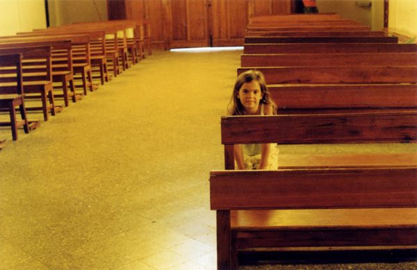 Young girl sitting alone in a wooden church pew