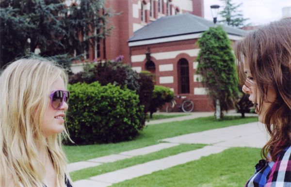 Two young people talking outside on a lawn near a brick building
