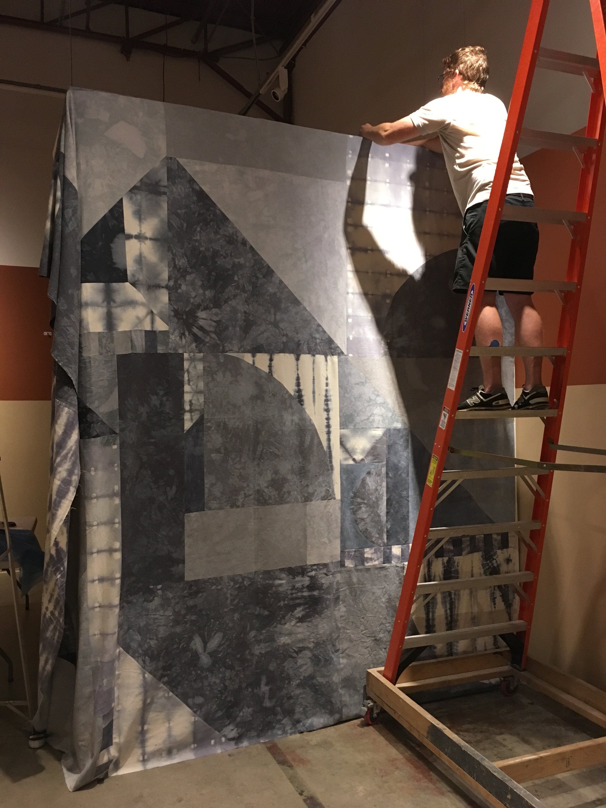 Worker on ladder installing large geometric-patterned wall hanging