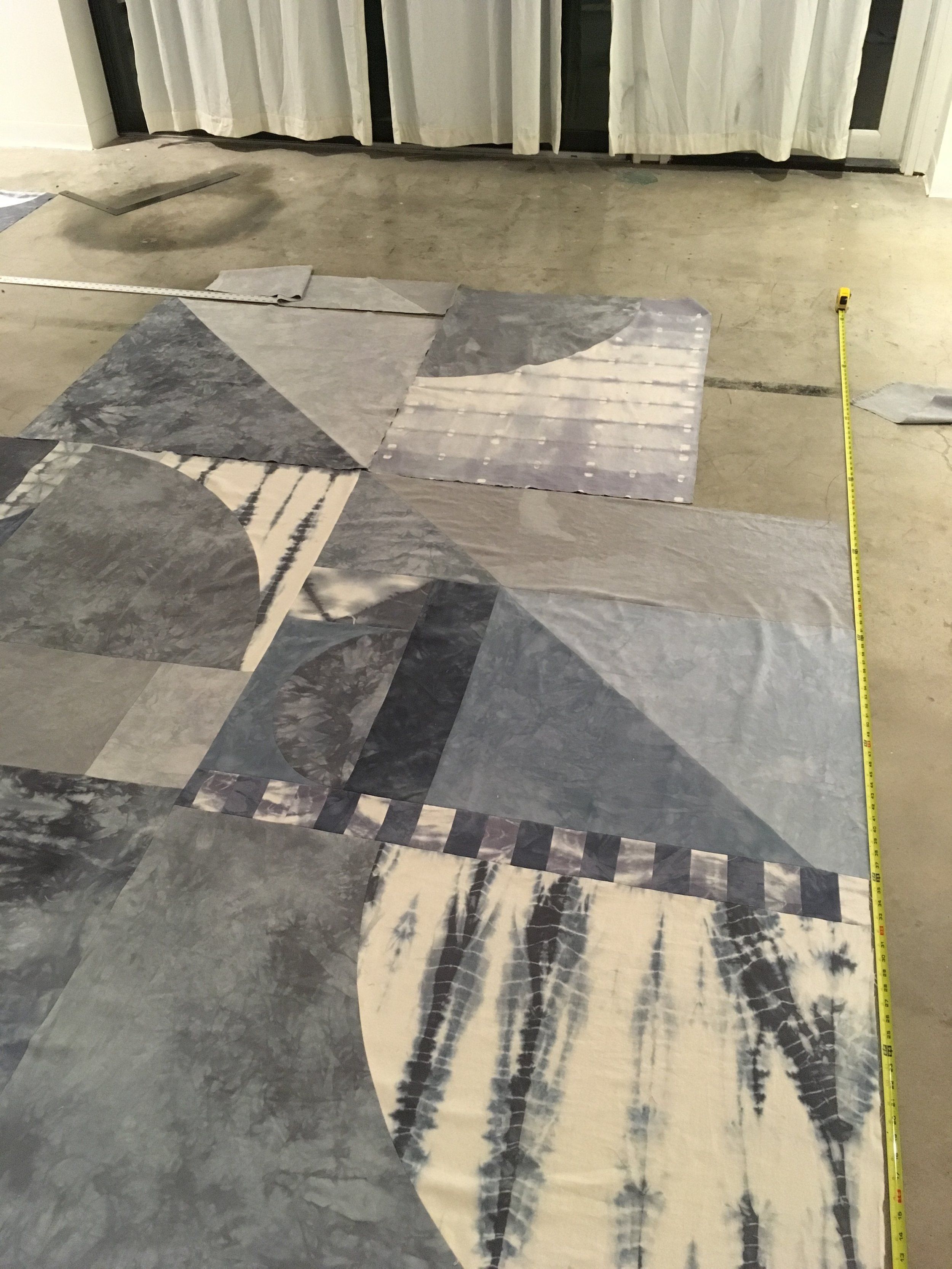 Large geometric patchwork textile laid on concrete floor with measuring tape