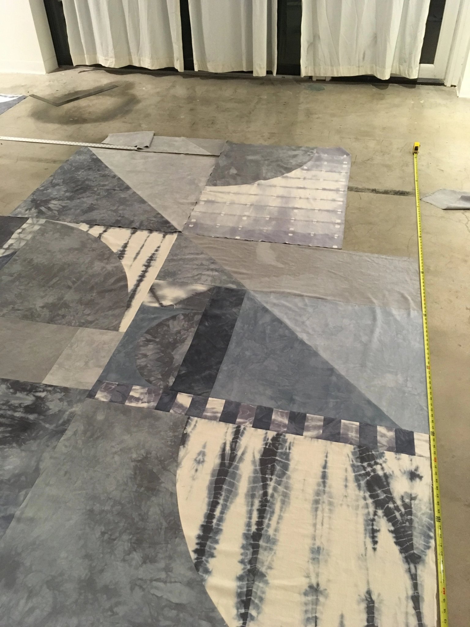 Large geometric patchwork textile laid on concrete floor with measuring tape