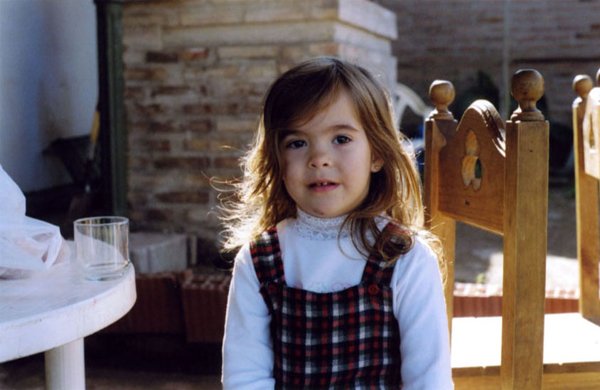 Young girl in plaid dress sitting on a wooden chair outdoors
