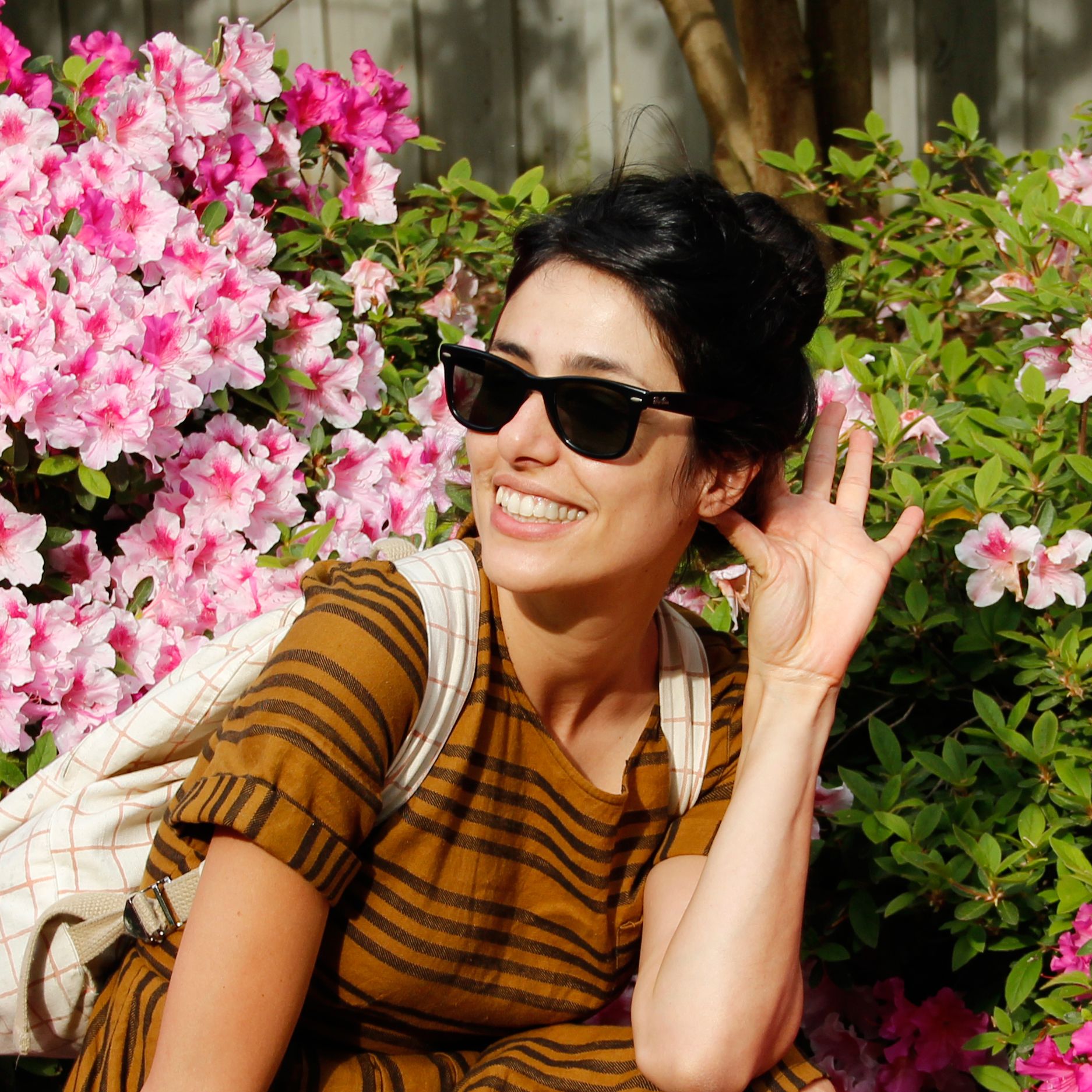 Smiling woman with backpack sitting beside blooming pink azaleas