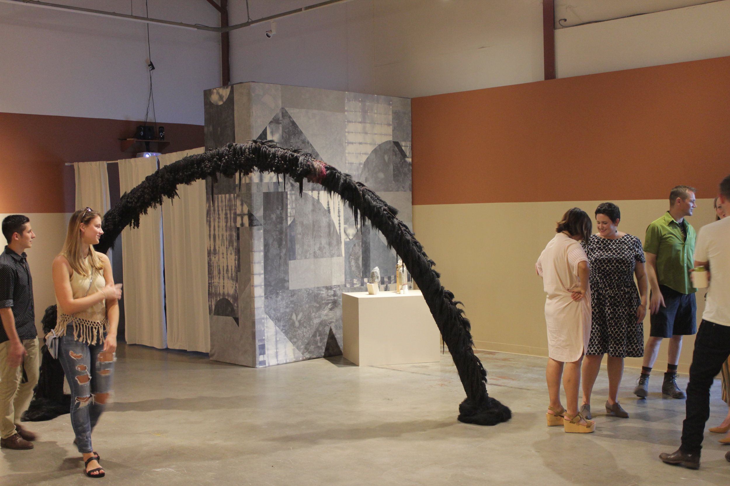 Visitors viewing a large black arched sculpture in a gallery