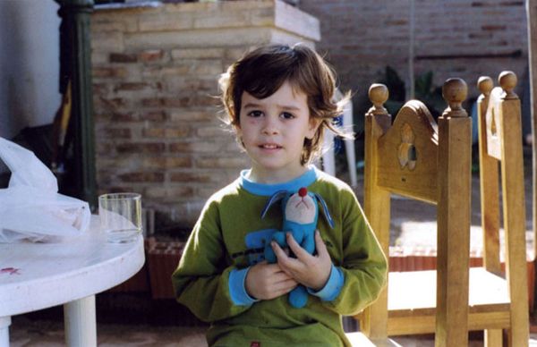 Young child sitting outdoors holding a small blue stuffed toy