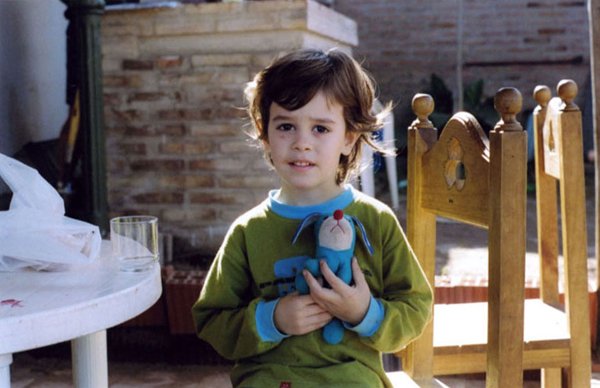 Young child sitting outdoors holding a small blue stuffed toy
