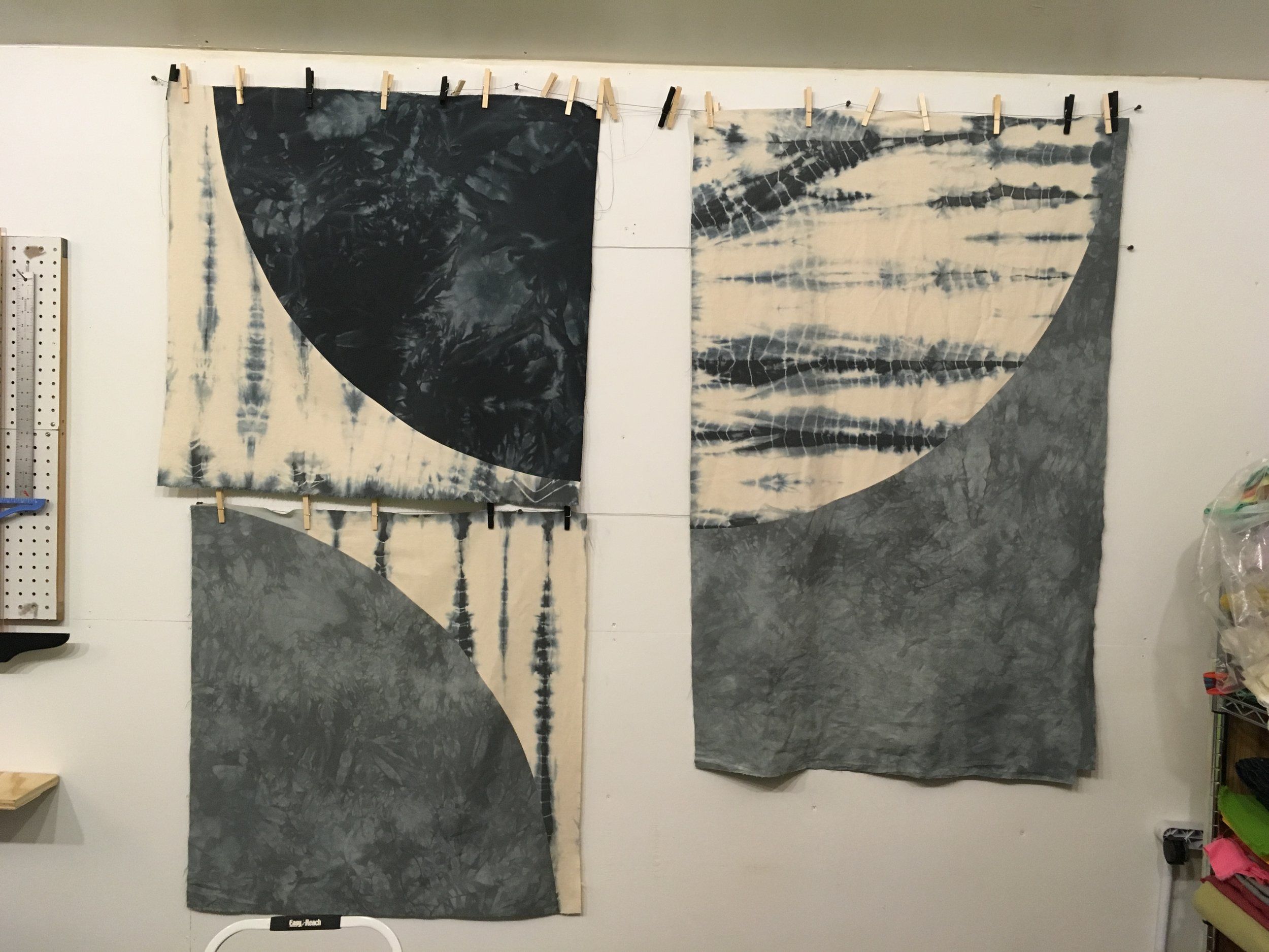 Three large tie-dyed fabric panels with curved shapes hanging on wall