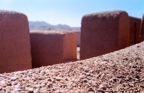 Close-up of textured adobe wall with surrounding earthen structures and distant hills