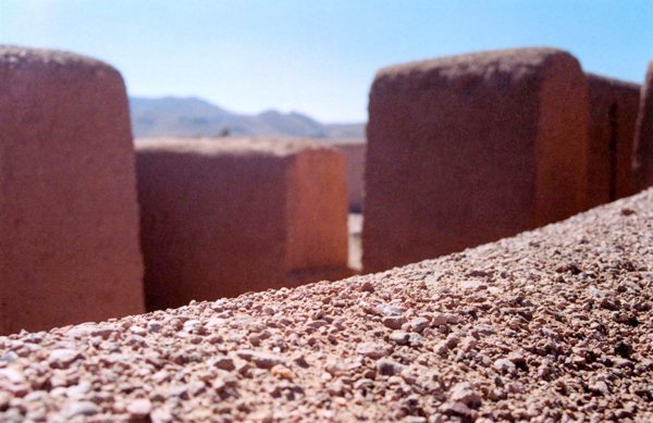 Close-up of textured adobe wall with surrounding earthen structures and distant hills