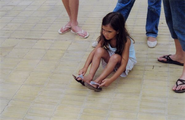 Young girl sitting on pavement putting on her flip-flops