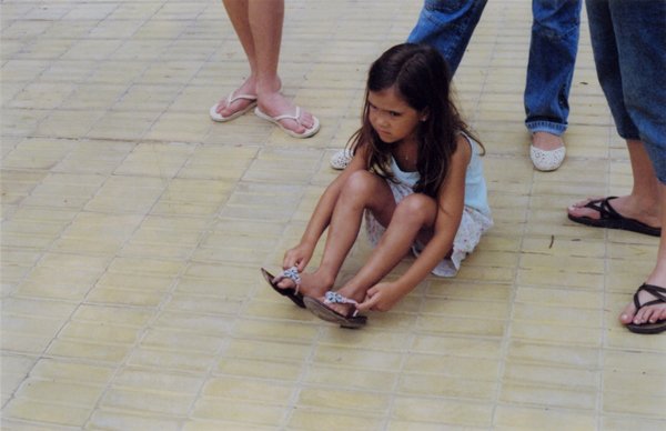 Young girl sitting on pavement putting on her flip-flops