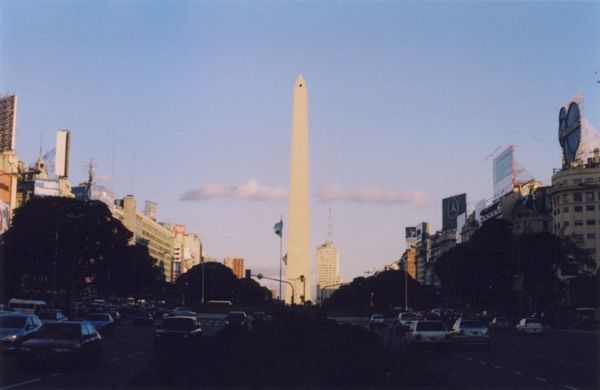 Tall obelisk standing in the middle of a busy city avenue