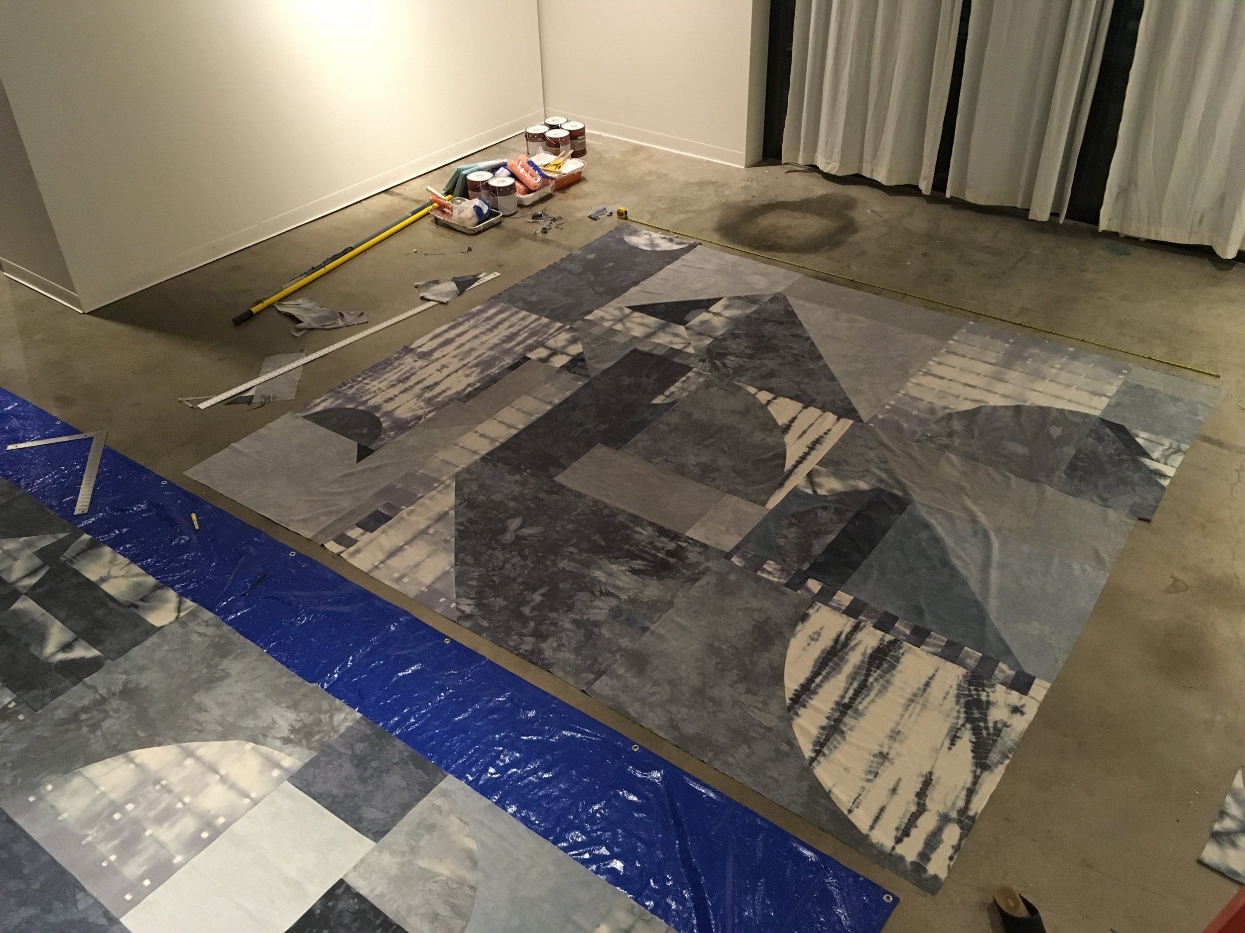 Large geometric mural being assembled on a gallery floor with tools nearby