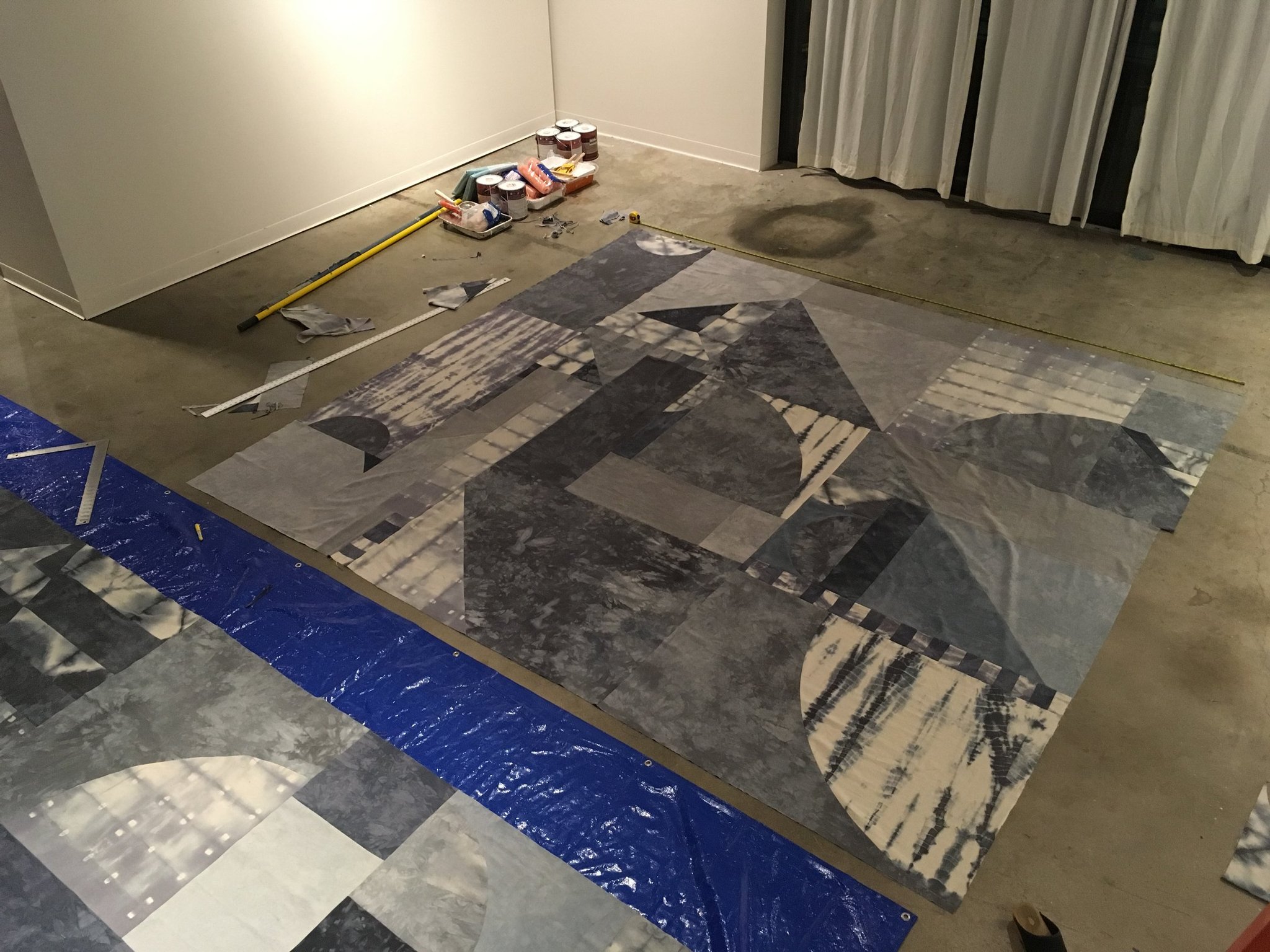 Large geometric mural being assembled on a gallery floor with tools nearby