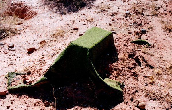 Green artificial turf draped over a low mound in desert soil