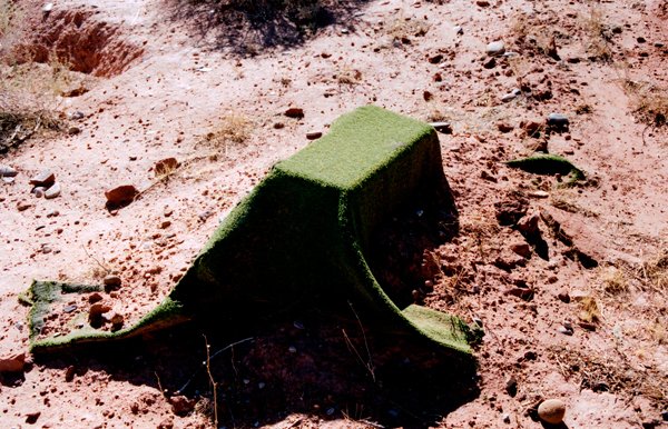 Green artificial turf draped over a low mound in desert soil