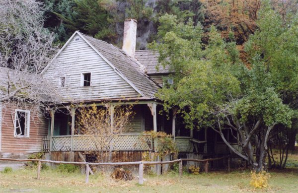 Old wooden house with wraparound porch surrounded by overgrown trees