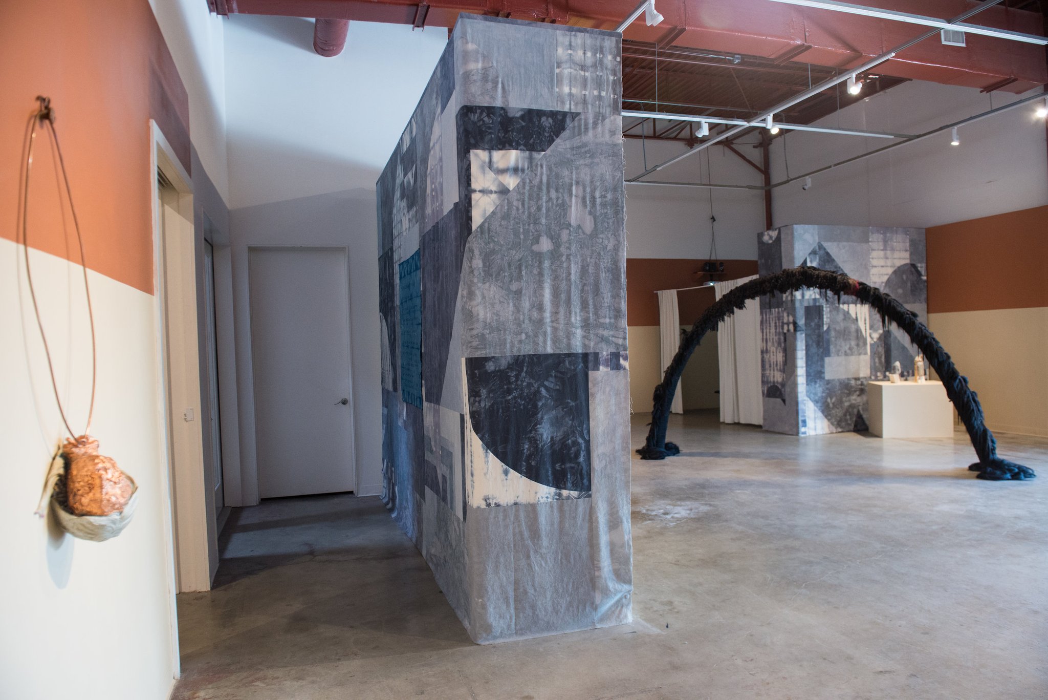 Contemporary gallery space with large fabric-covered structures and arched sculpture