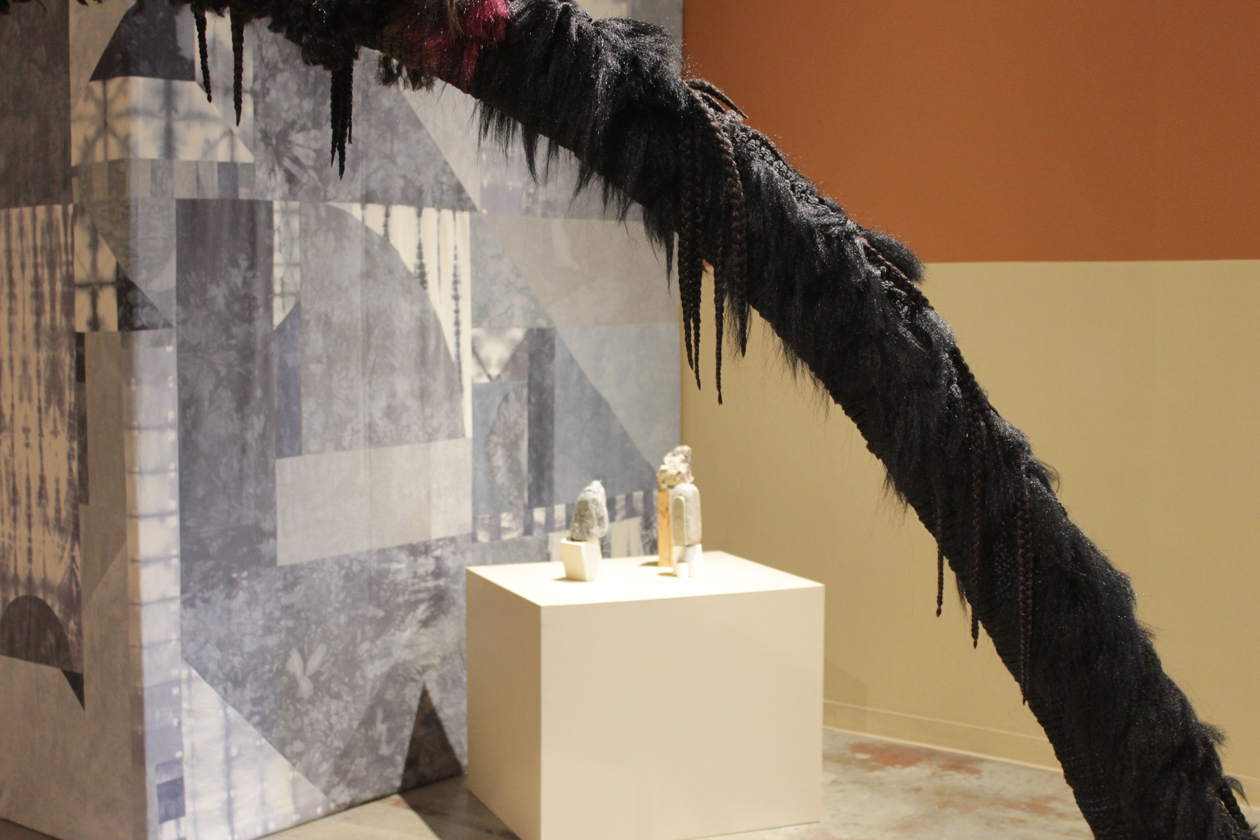 Art gallery installation with braided black arch over small sculptures