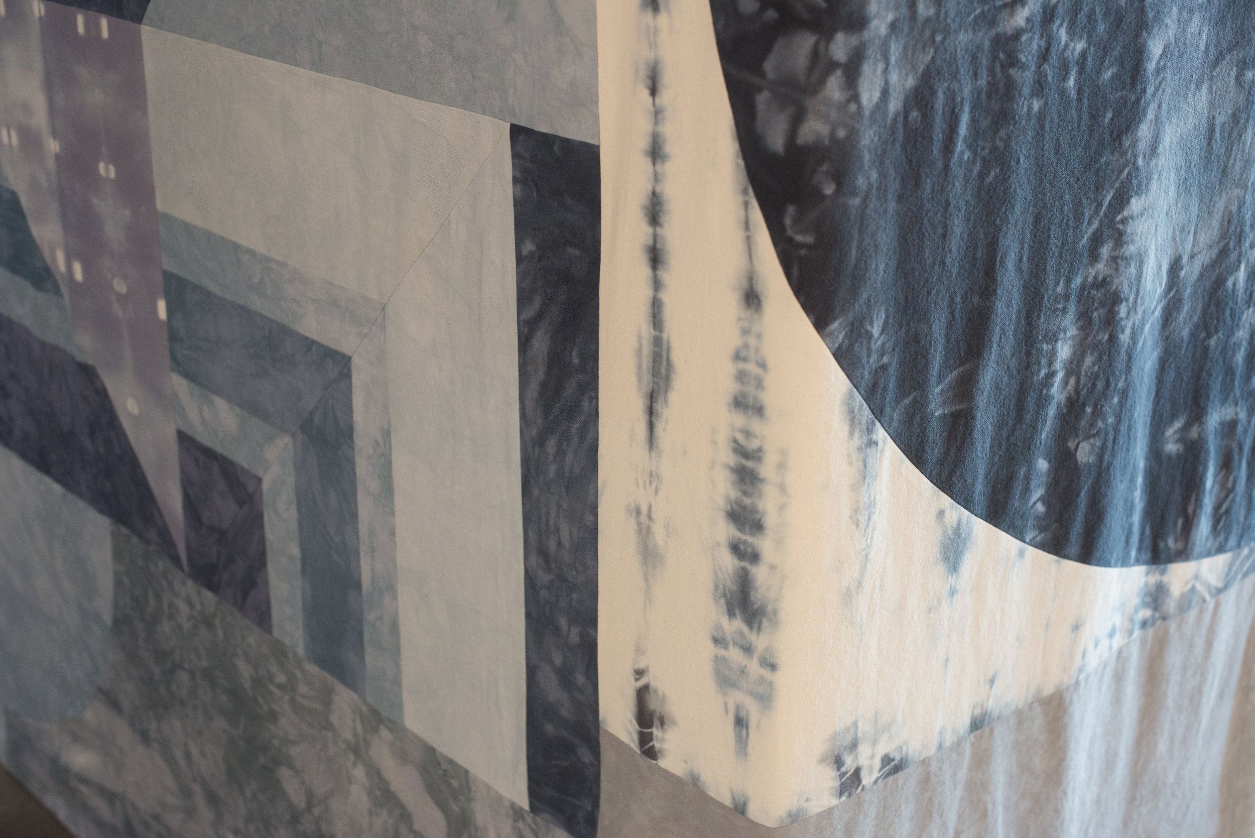 Abstract textile artwork with geometric shapes and blue tie-dye patterns