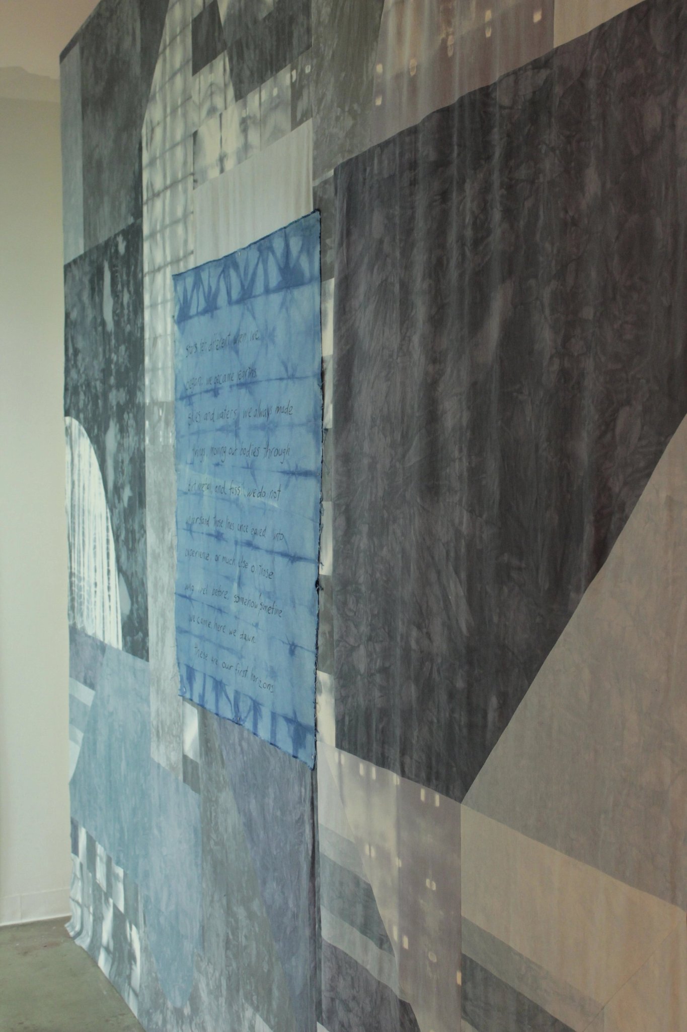 Large abstract wall hanging with layered geometric panels and faint text
