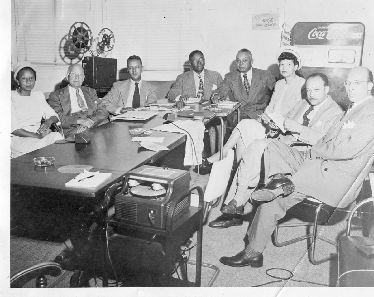 Faded black and white photo of men in suits sitting around a conference table