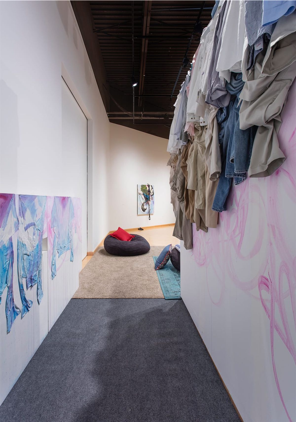 Installation view from inside narrow hallway with uniform clothing overhead on wall to the left