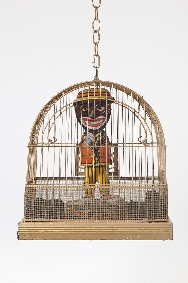Standing miniature male figure in blackface glaring out from inside birdcage