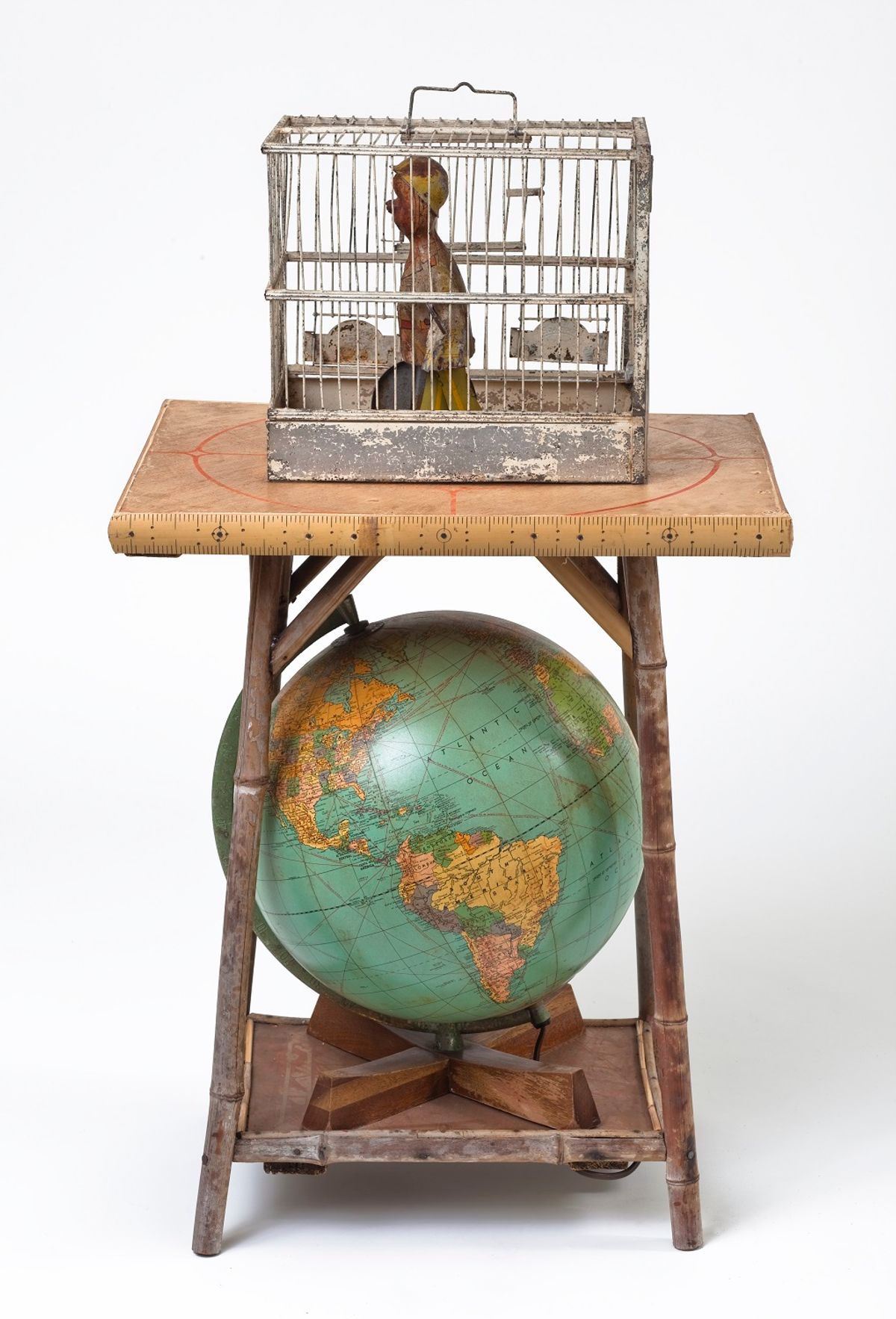 Assemblage of human figure in birdcage atop a small table with a globe underneath