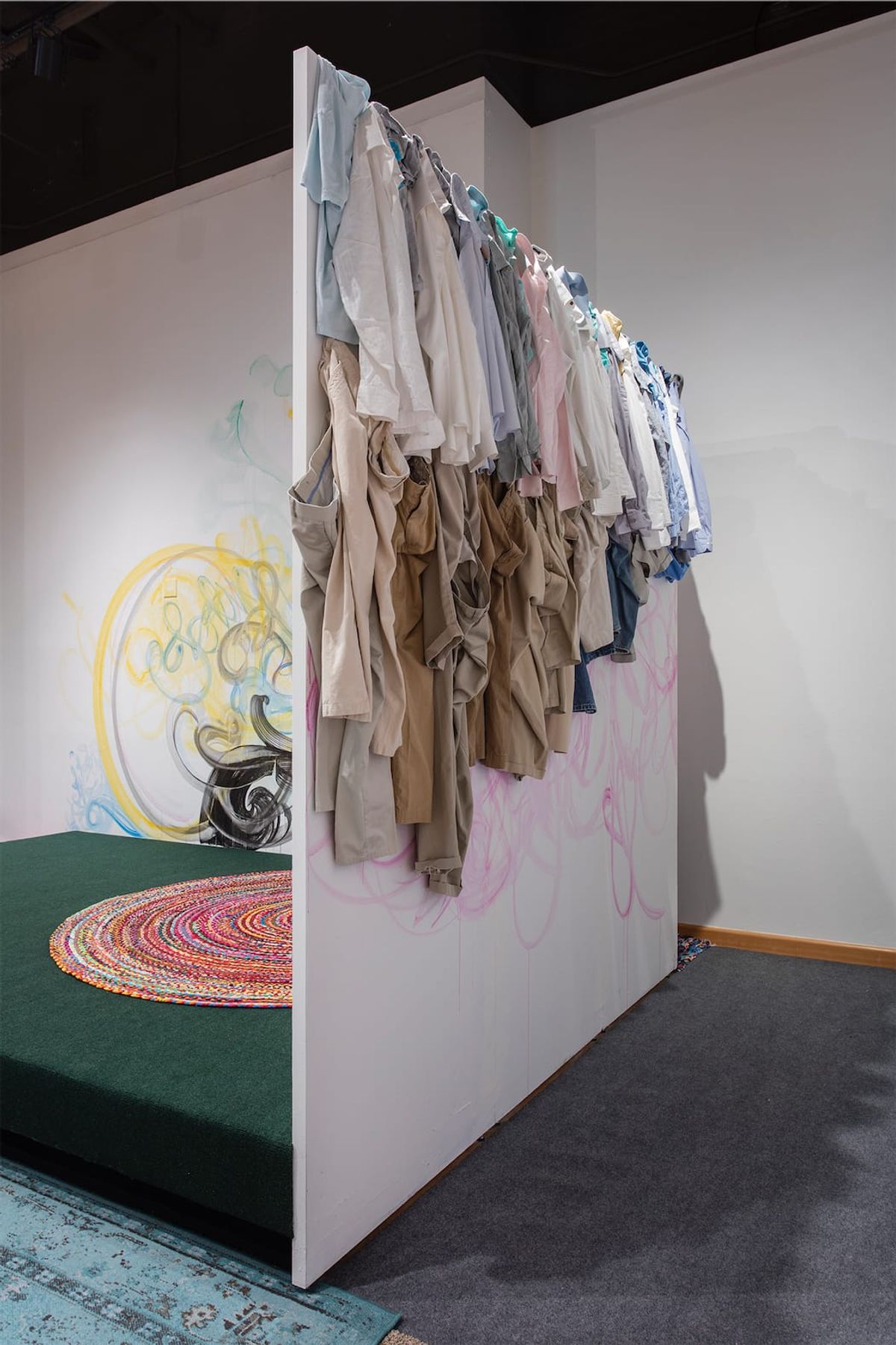 Installation view of uniform khakis and pastel shirts at entrance to soft space vignette