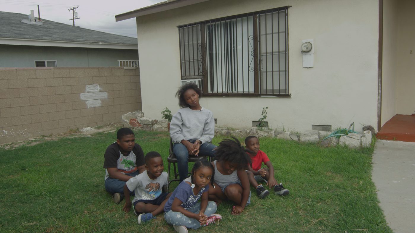 Family gathered for portrait on green lawn in front of house with bars on the windows