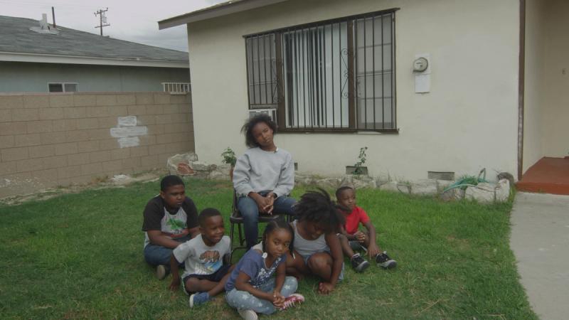 Family gathered for portrait on green lawn in front of house with bars on the windows