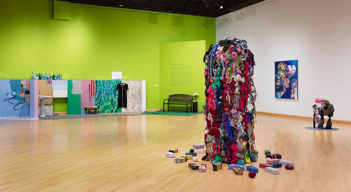 Installation view with focus on tall sculpture of bundled clothing in center of space