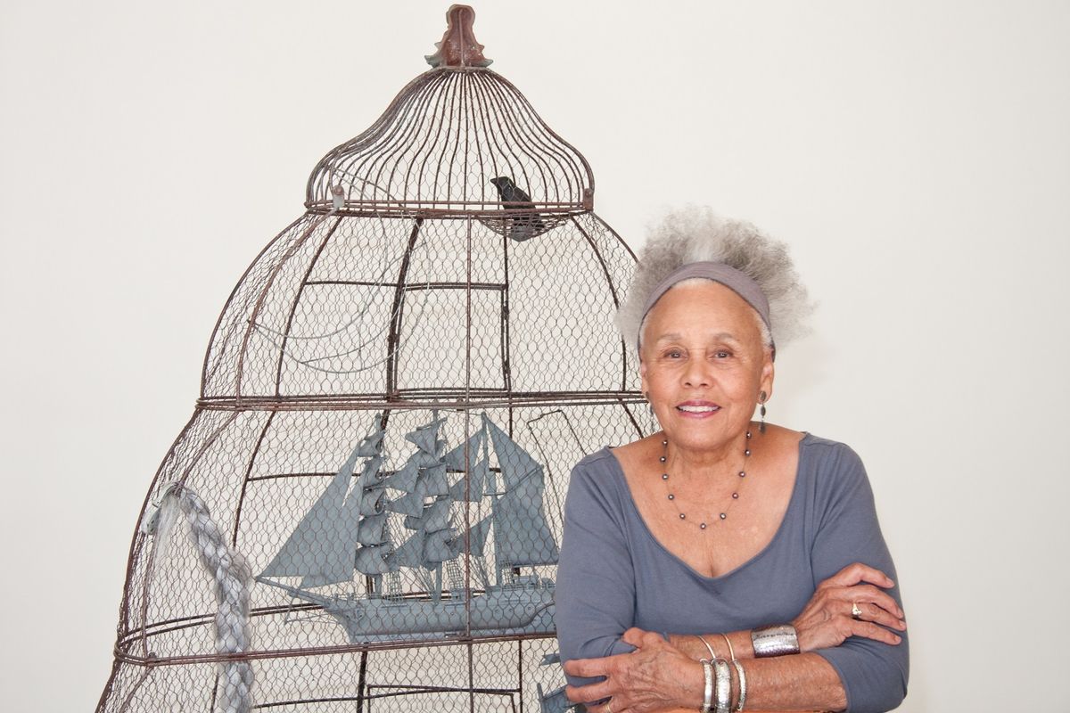 Portrait of Betye Saar in front of large bird cage