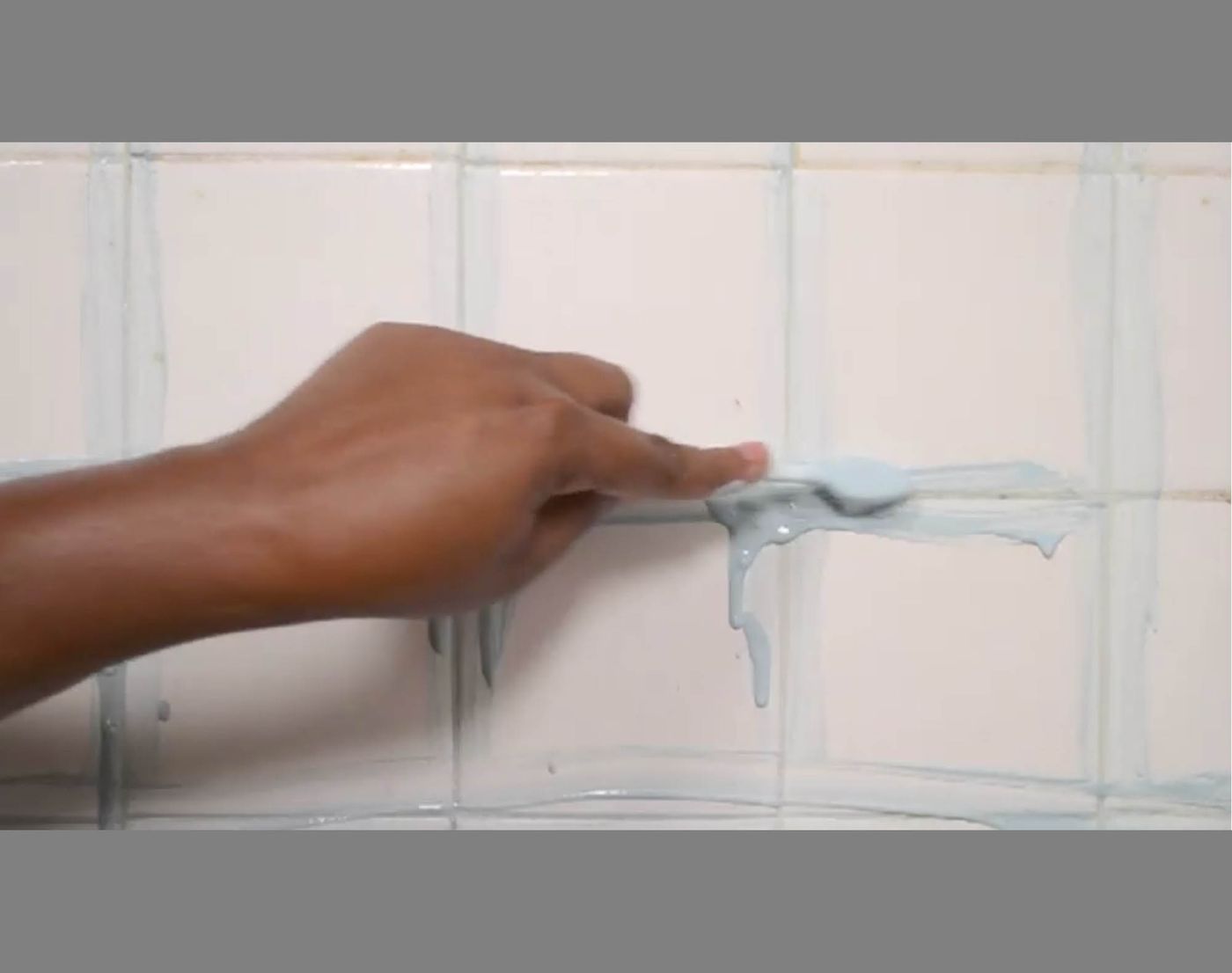 Hand with tool applying scrubbing cleanser to shower tiles