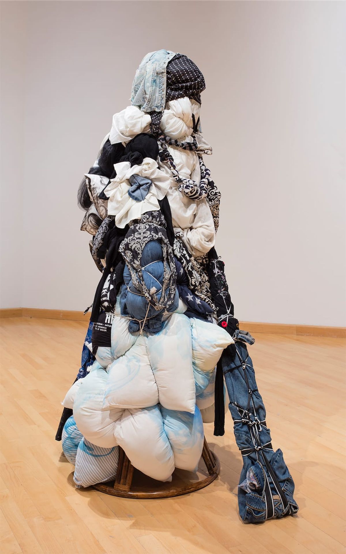 Installation view of human figure made of stuffed bags carrying more bags