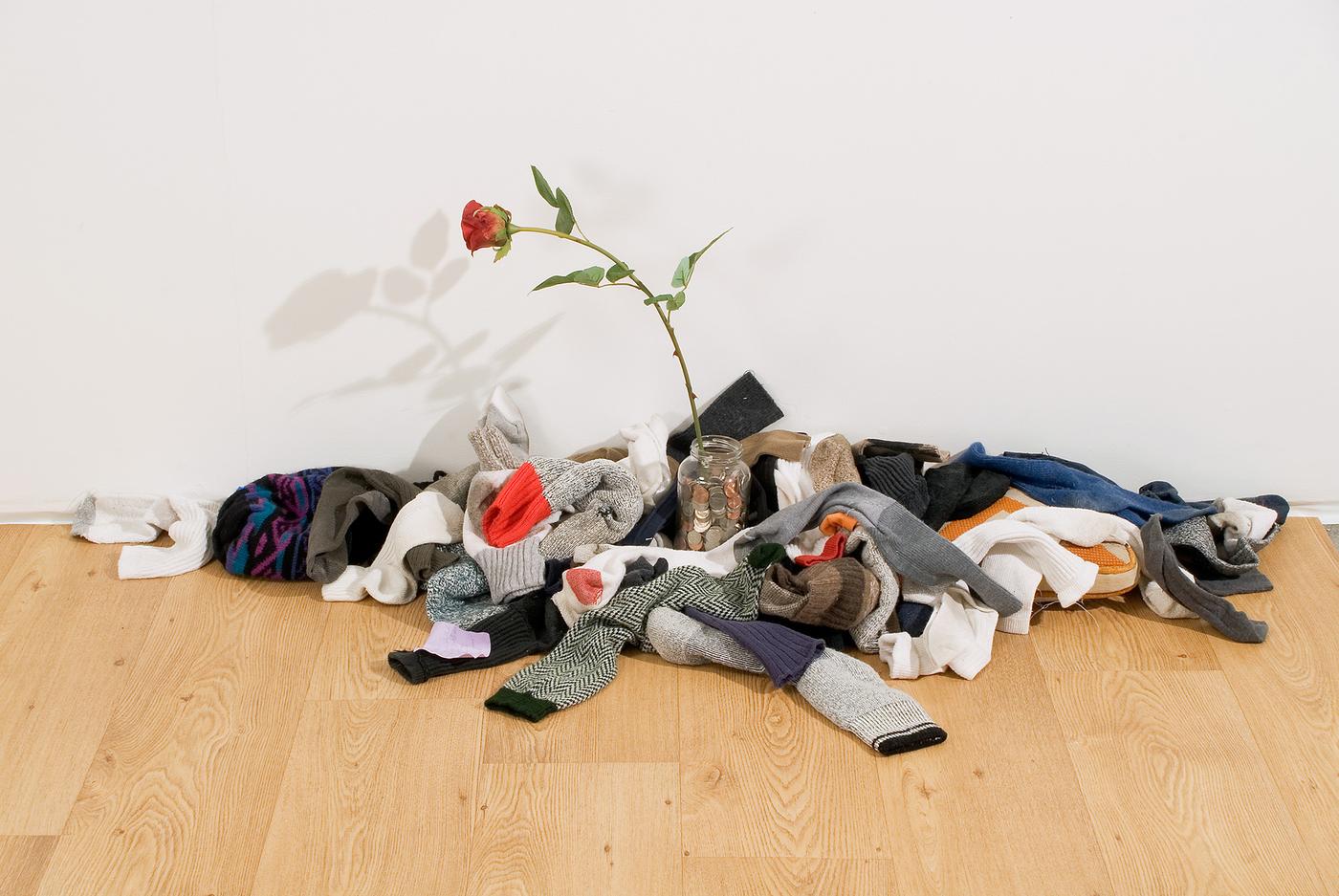 Installation view of jumbled clothing with a rose in the middle