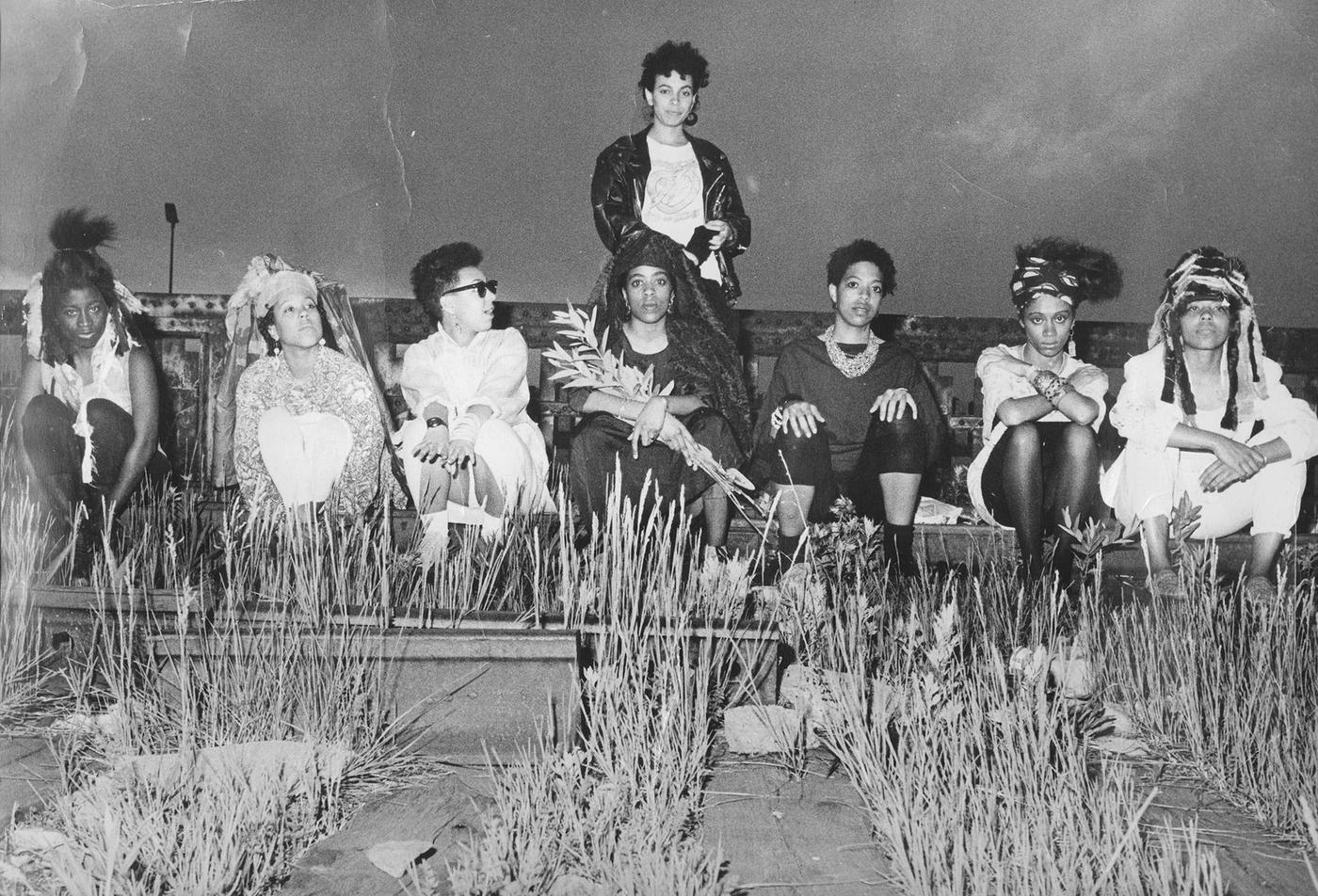 Black and white photo of eight black women seated amongst wildflowers