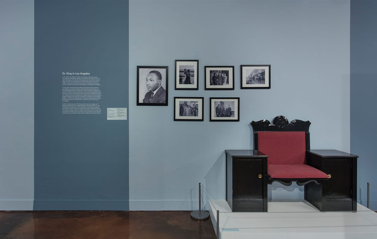 Installation view of red chair, wall text, and framed photos