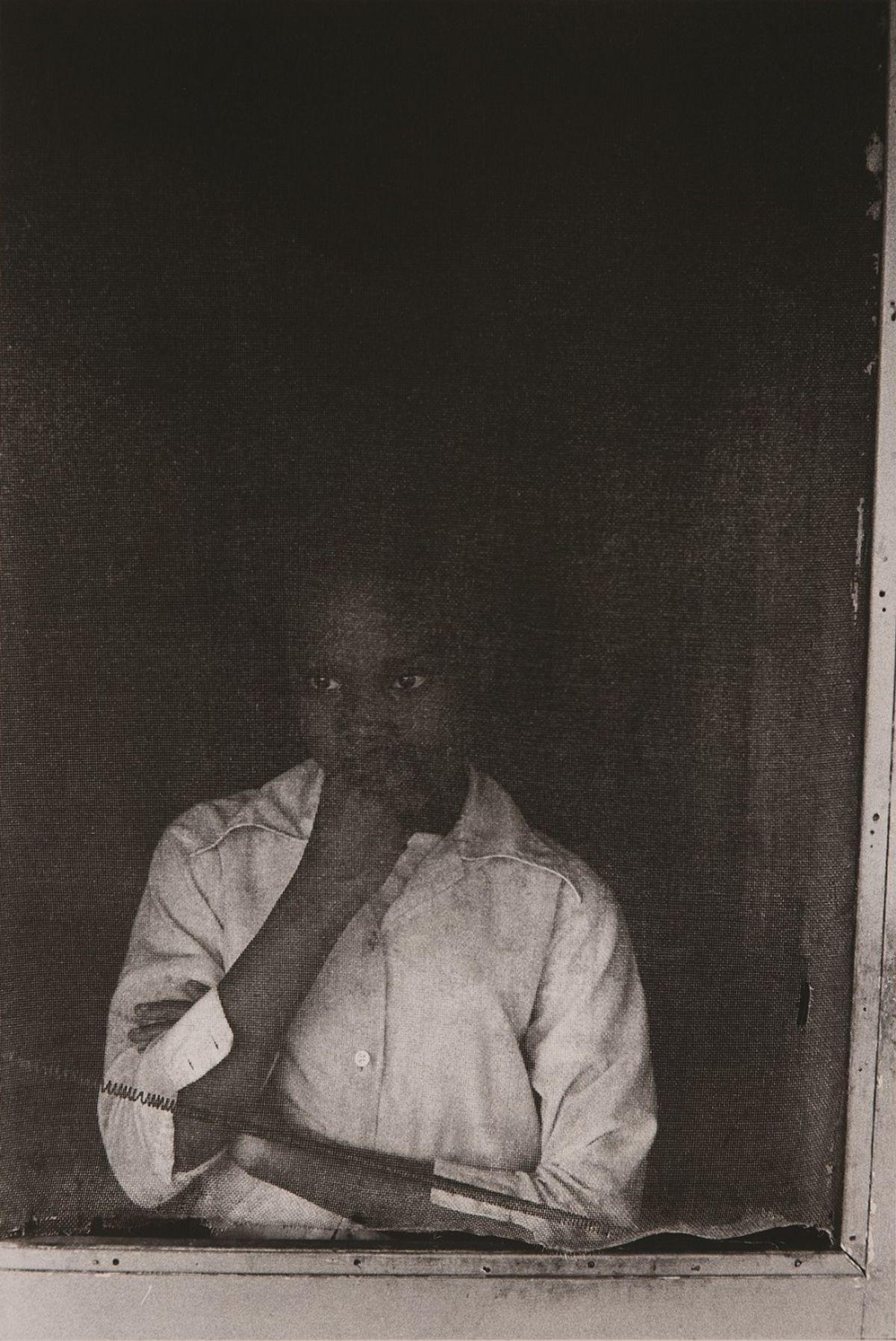 Girl with arms folded looking out from behind screen door