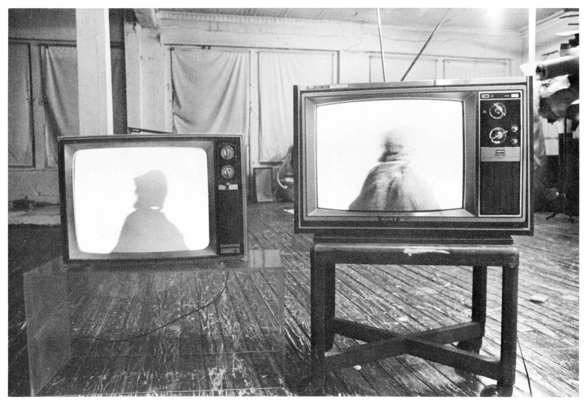 Black and white photograph of two televisions playing side by side in large empty living space