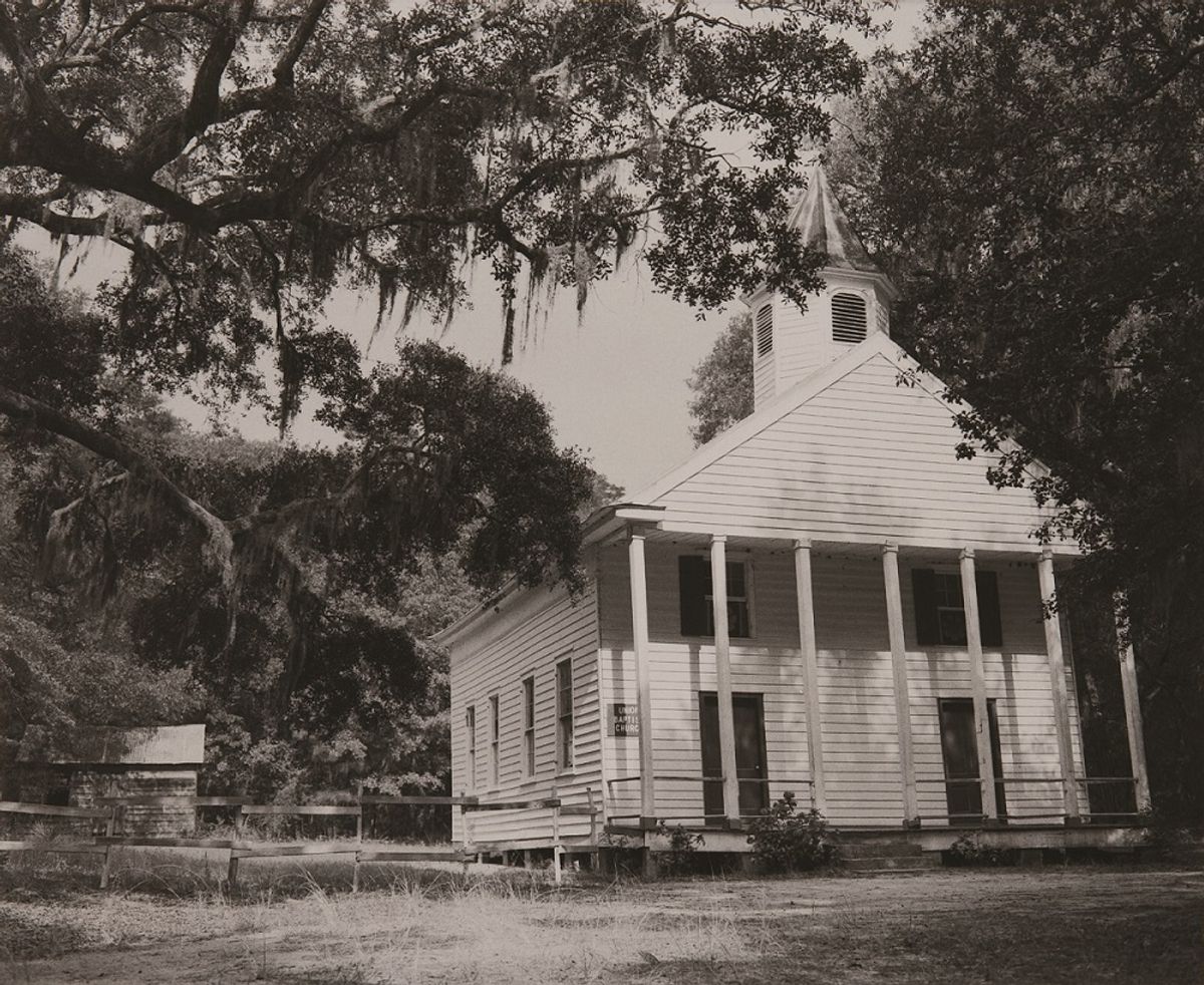 White, slat, wood church building viewed in distance through frame of tree branches