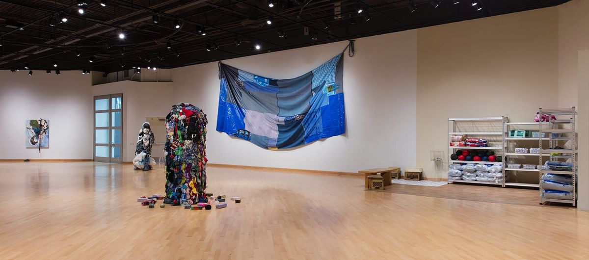 Installation view of bundled clothing, work room vignette, and blue patchwork