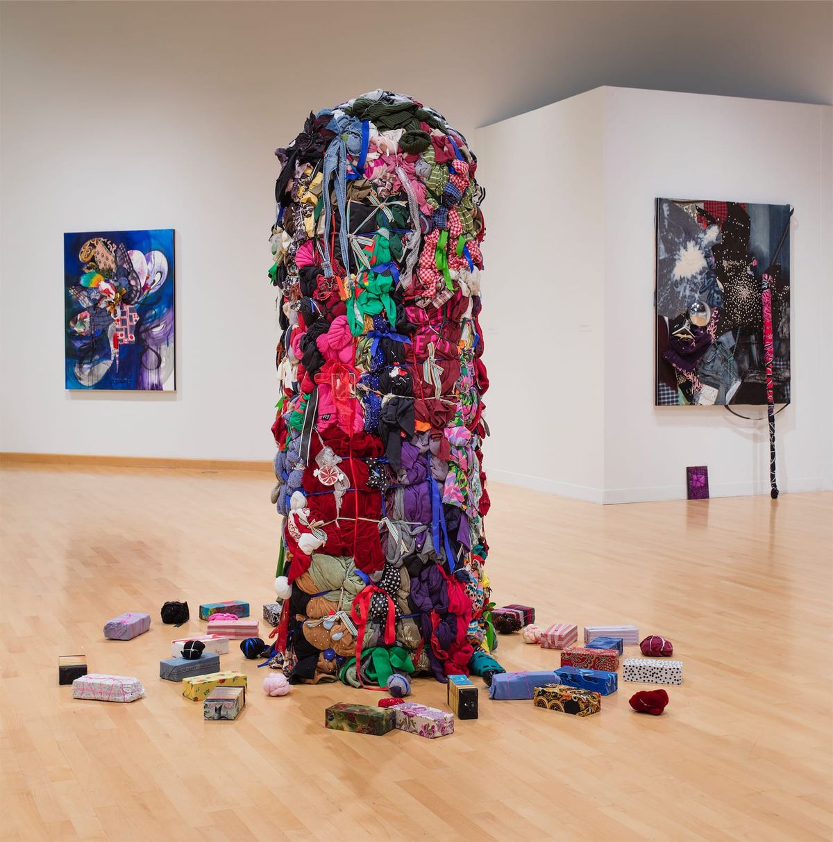 Installation view with focus on tall sculpture of bundled clothing in center of space
