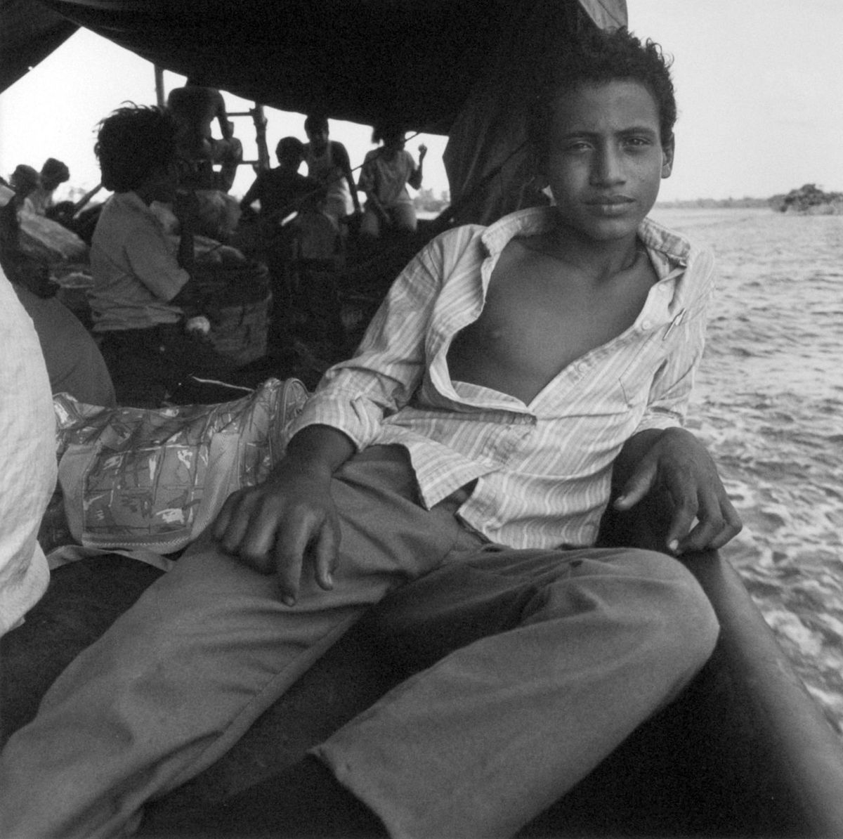 Black and white photo of seated boy on crowded boat