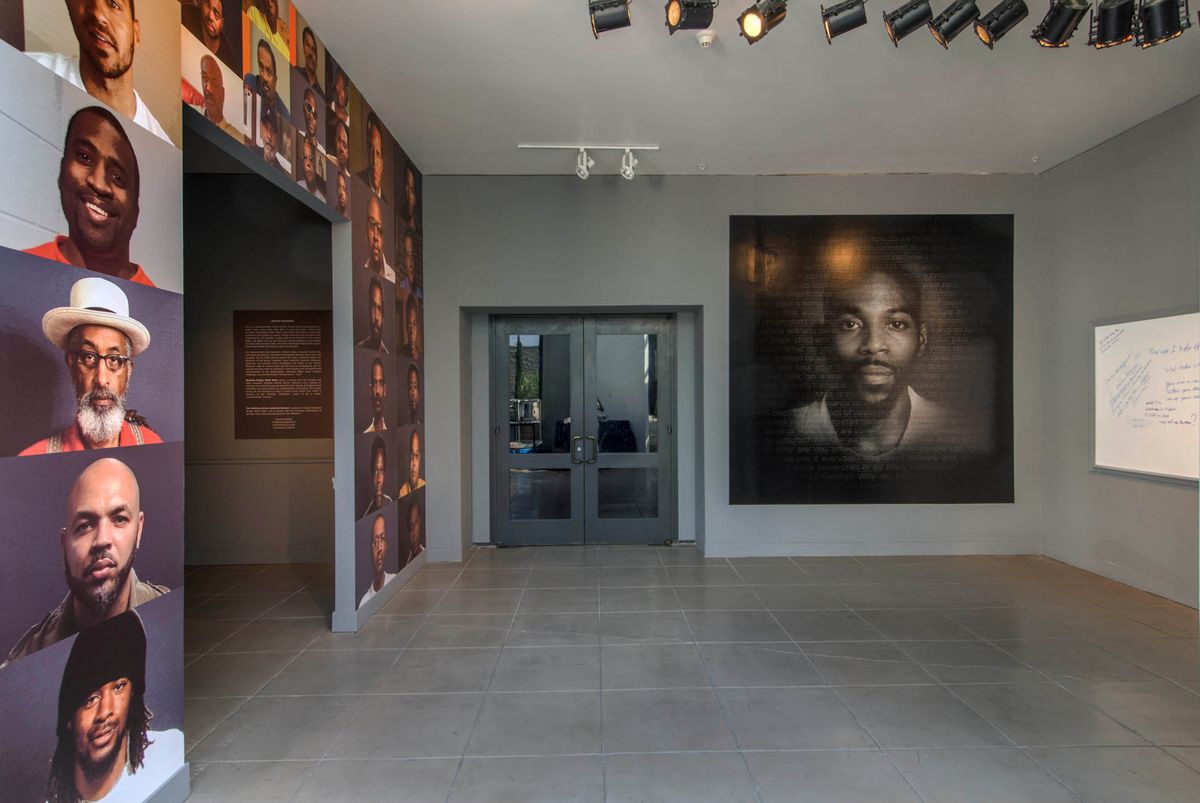 Installation view of room papered with photos of dozens of Black men's faces