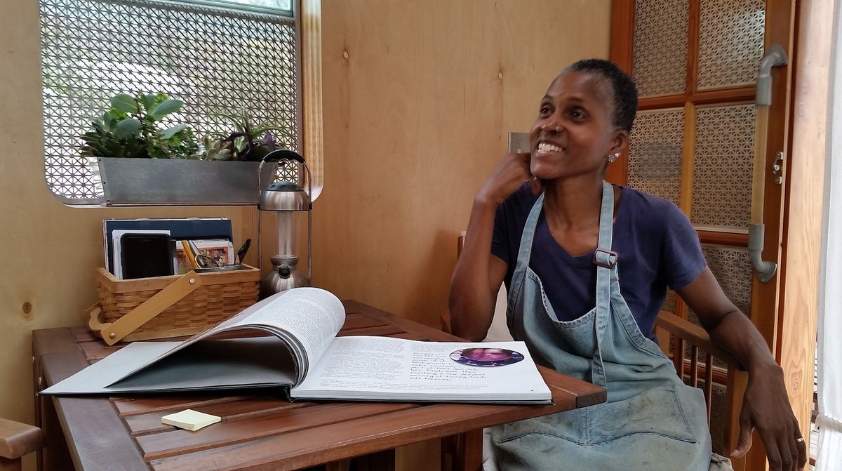 Artist, Dominque Moody seated at table with large book open