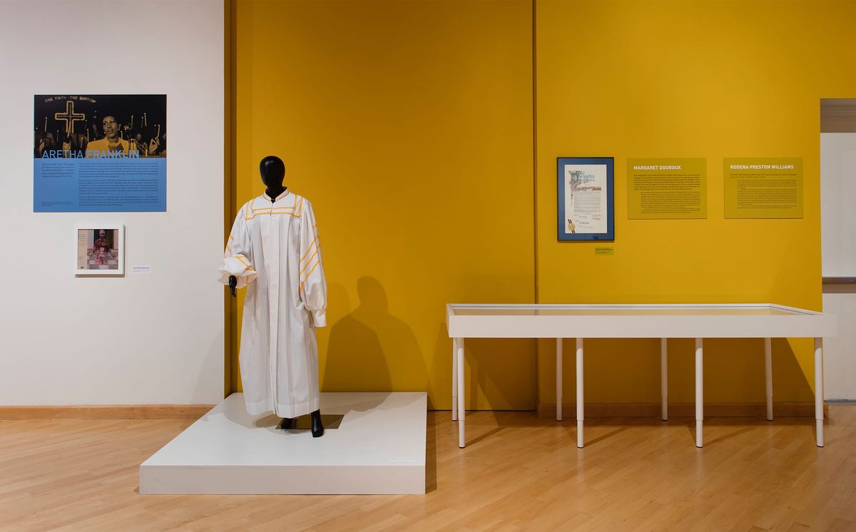 Installation view or choir robe, vitrine, monitor, and photo elements