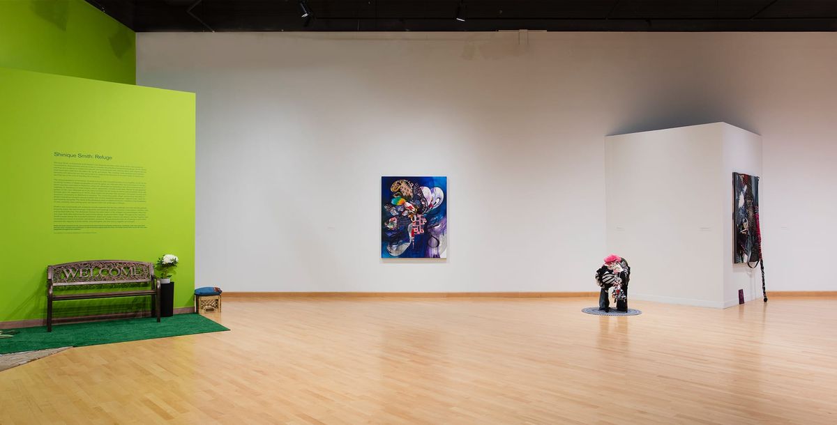 Installation view of sparsely distributed paintings, bench, wall text, and sculpture